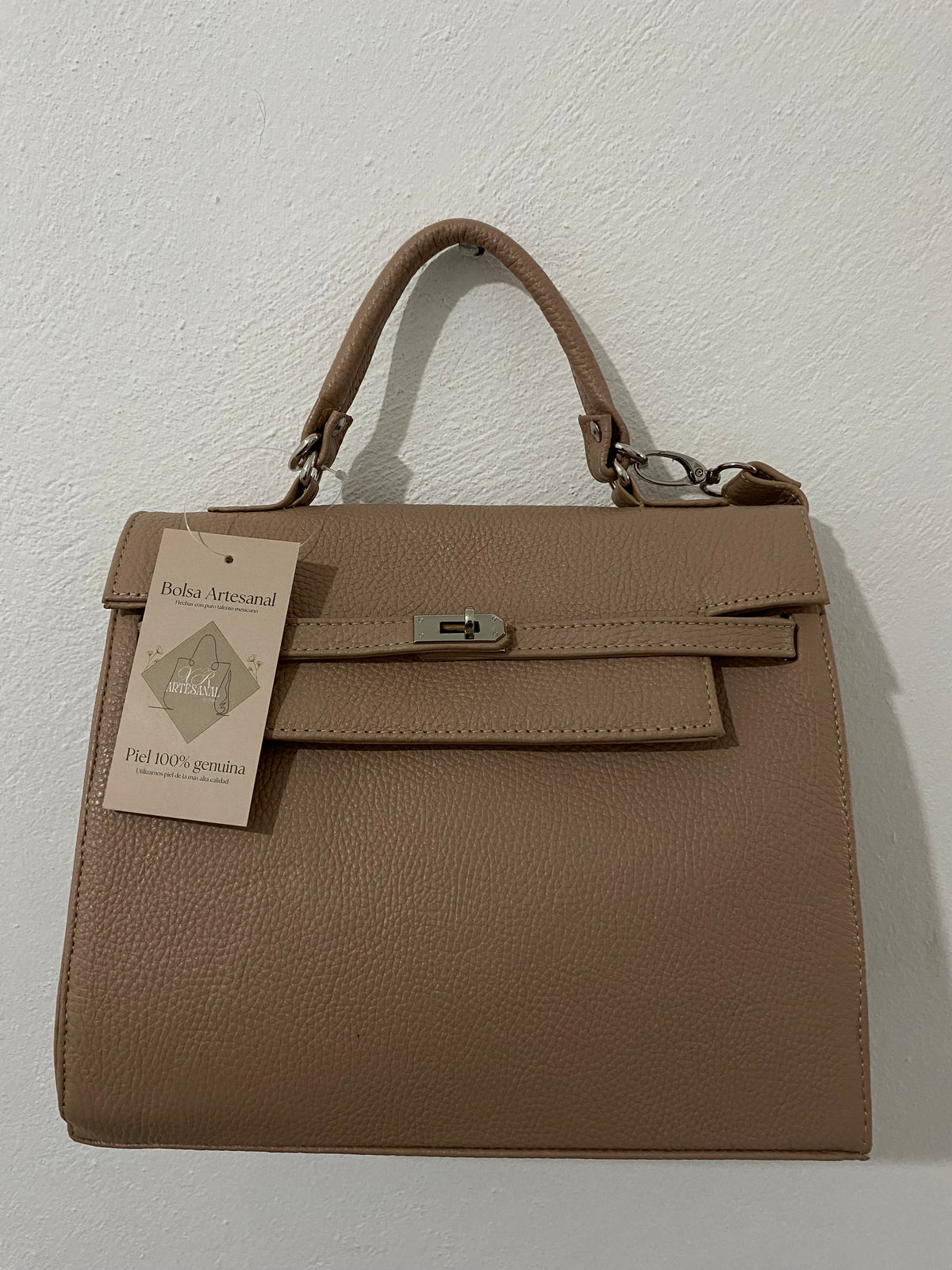 Bolsa Kelly Taupe colgada vista frontal con etiqueta artesanal